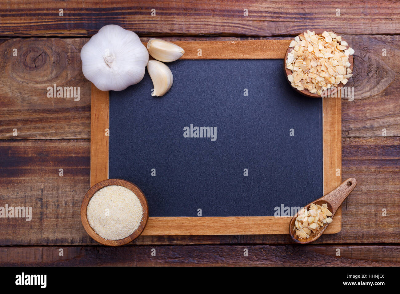 garlic cloves, bulb, flakes and powder on old wooden background with black board for text Stock Photo