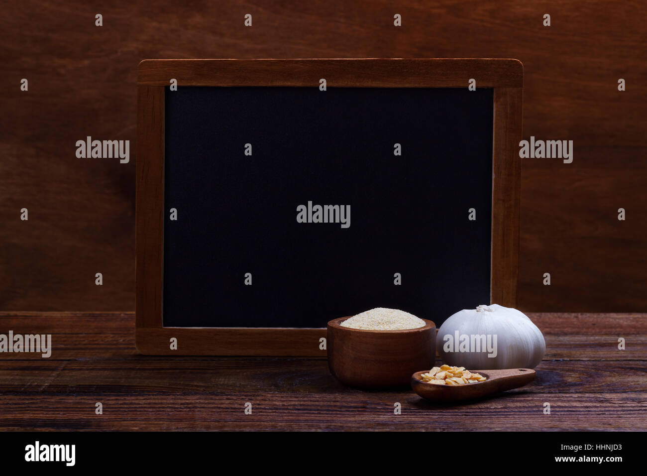 garlic cloves, bulb, flakes and powder on old wooden background with black board for text Stock Photo