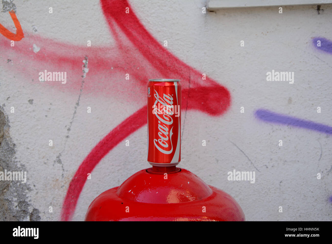 Venice, Italy - September 9, 2016: Coca Cola can standing on top of red hydrant at painted wall. Stock Photo