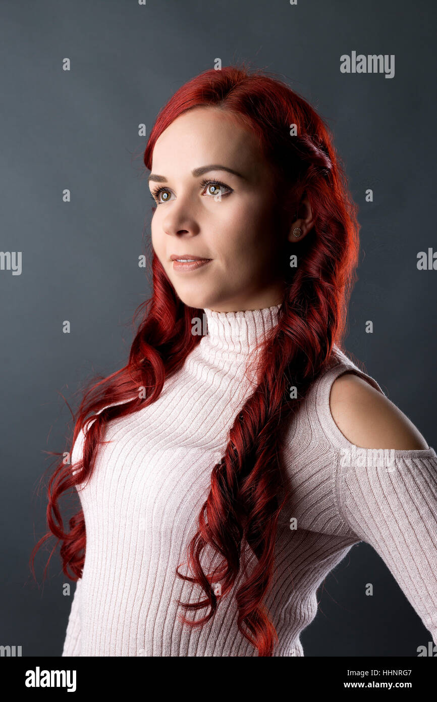 Portrait of young woman with long red hair, grey backdrop Stock Photo