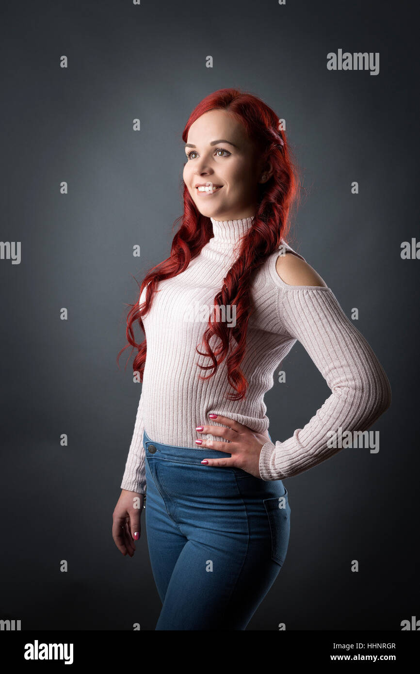 Three quarter length portrait of young woman with long red hair, grey backdrop Stock Photo