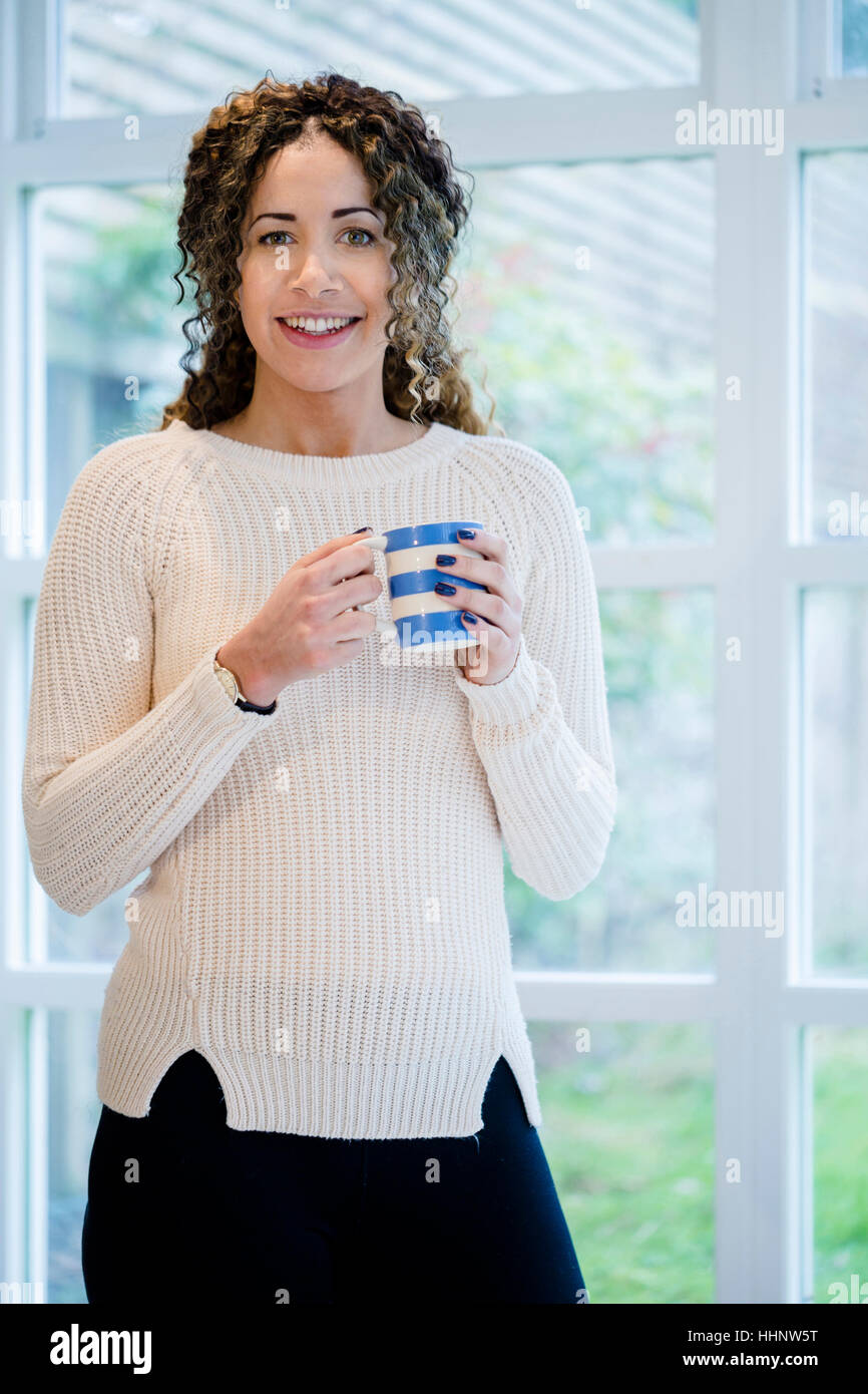 Woman standing near window holding coffee cup Stock Photo