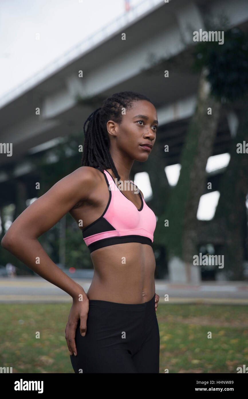 Serious Mixed Race woman wearing pink sports-bra near bridge Stock