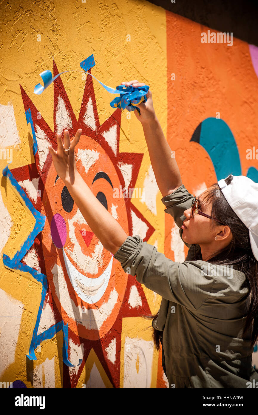 Woman removing painting tape from mural on wall Stock Photo