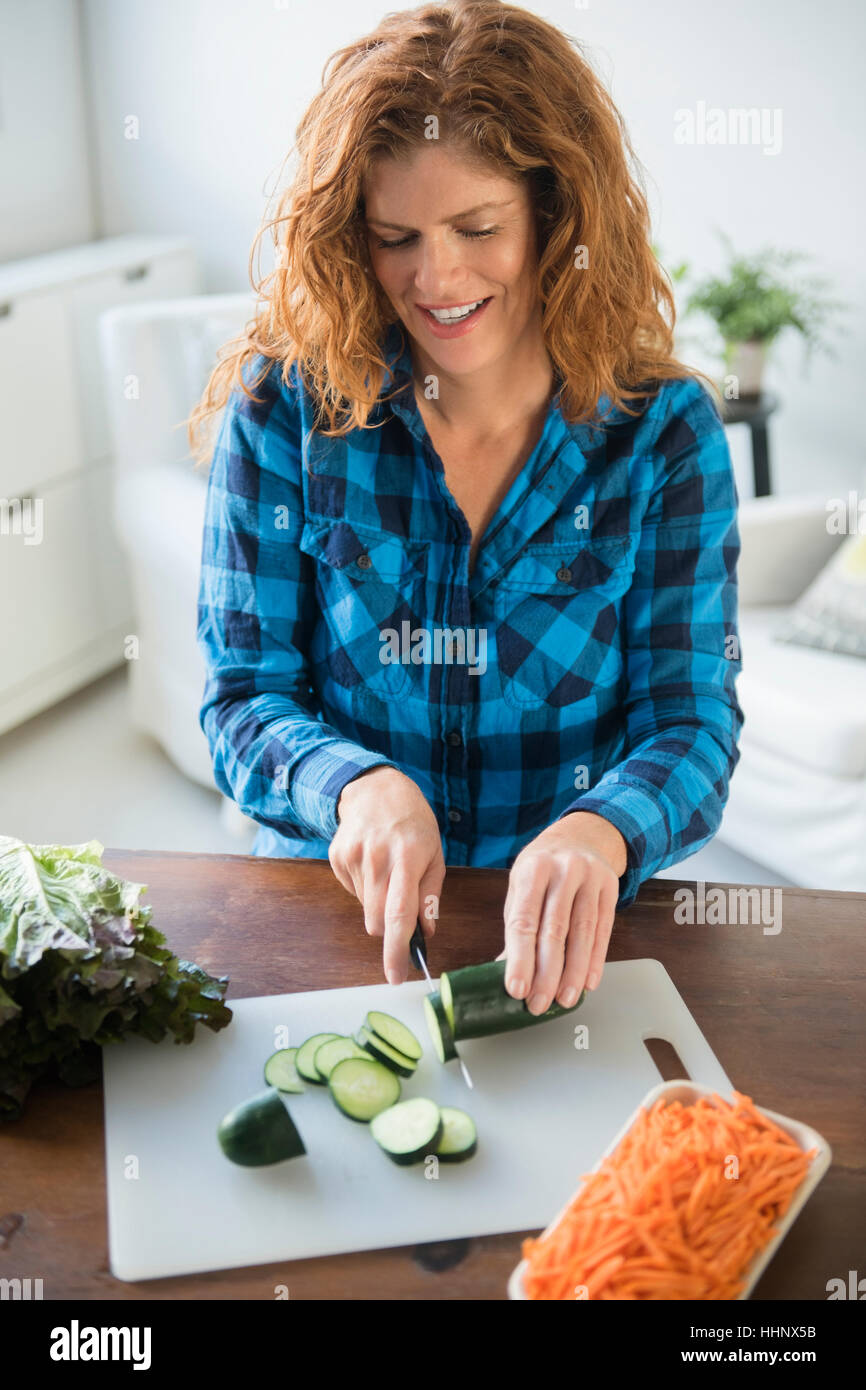 Smiling Caucasian woman slicing cucumbers Stock Photo