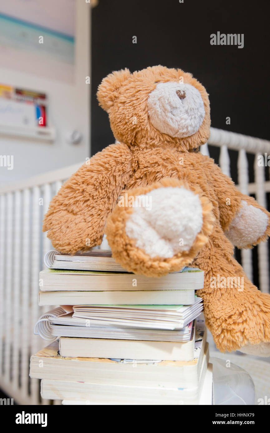 Teddy bear on stack of books near crib Stock Photo