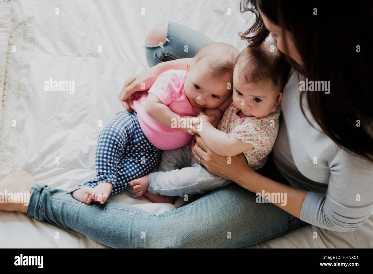 Caucasian mother sitting on bed holding twin baby daughters Stock Photo