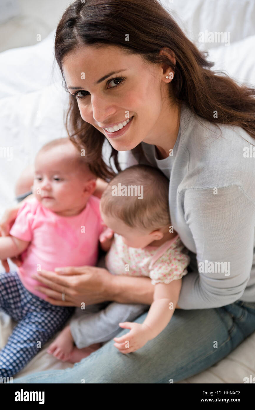 Caucasian mother sitting on bed holding twin baby daughters Stock Photo