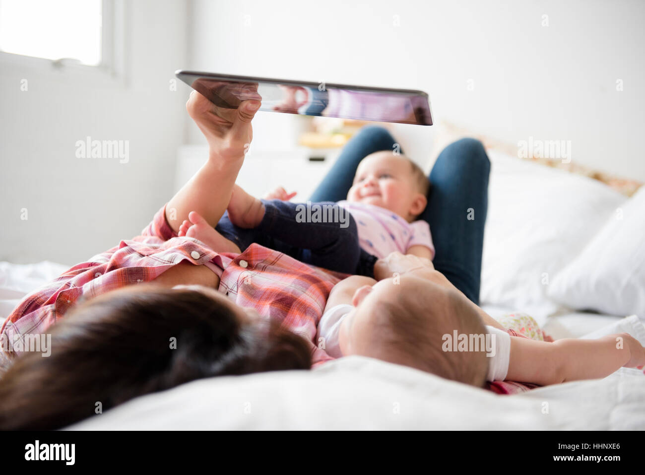 Caucasian mother on bed with twin baby daughters using digital tablet Stock Photo