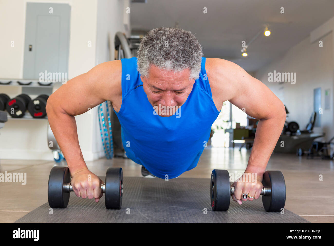 Mixed Race man doing push-ups with dumbbells in gymnasium Stock Photo
