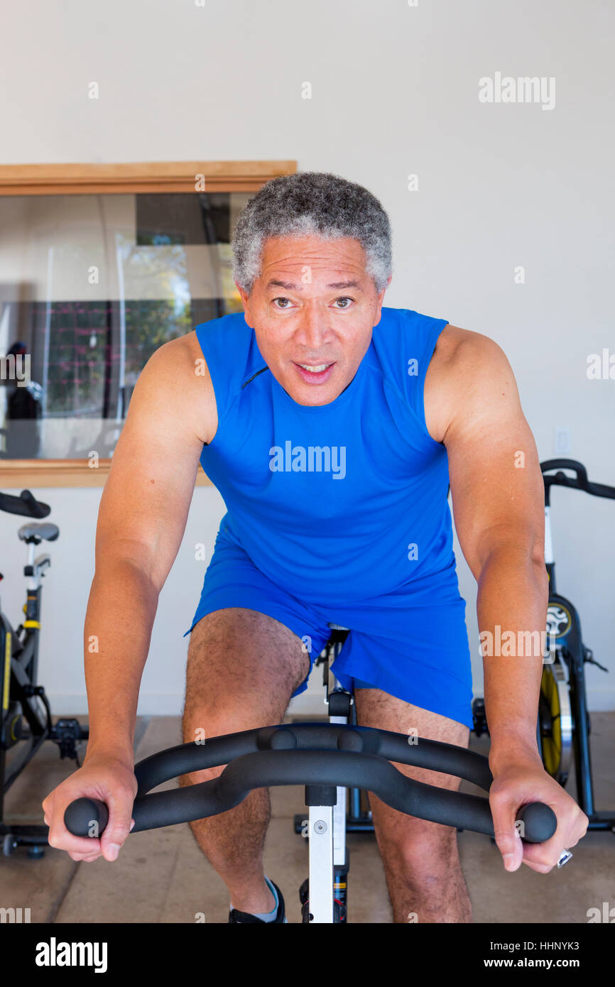Mixed Race man riding stationary bicycle in gymnasium Stock Photo