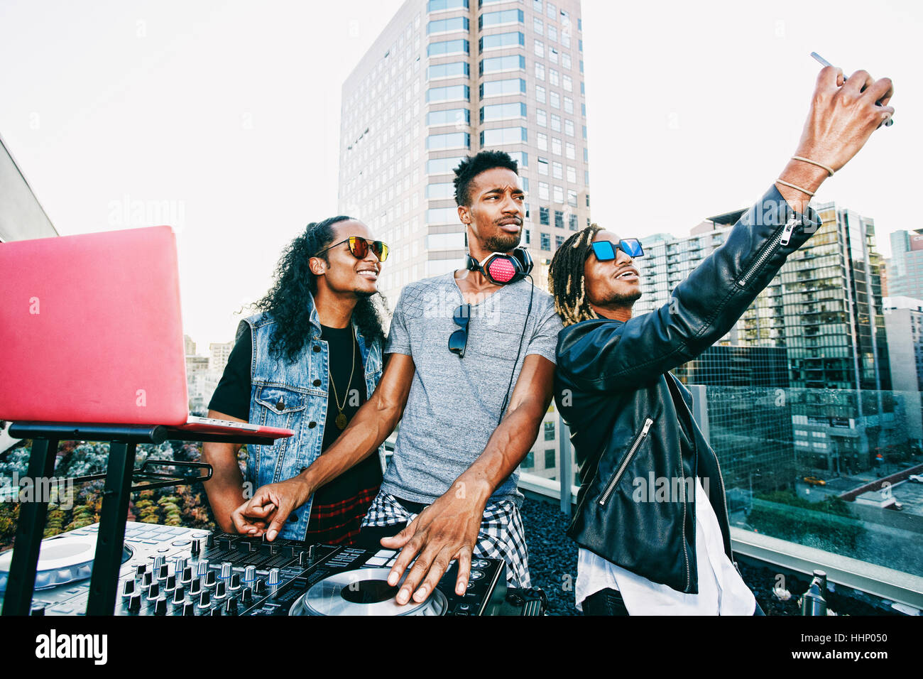 Men posing for cell phone selfie with DJ on urban rooftop Stock Photo