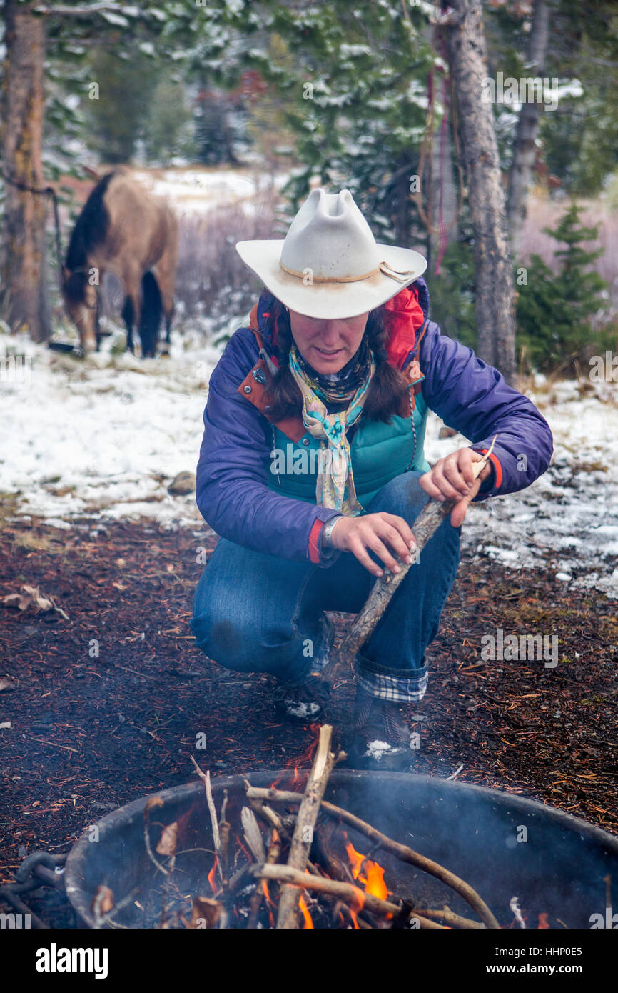 Caucasian woman putting wood in campfire Stock Photo