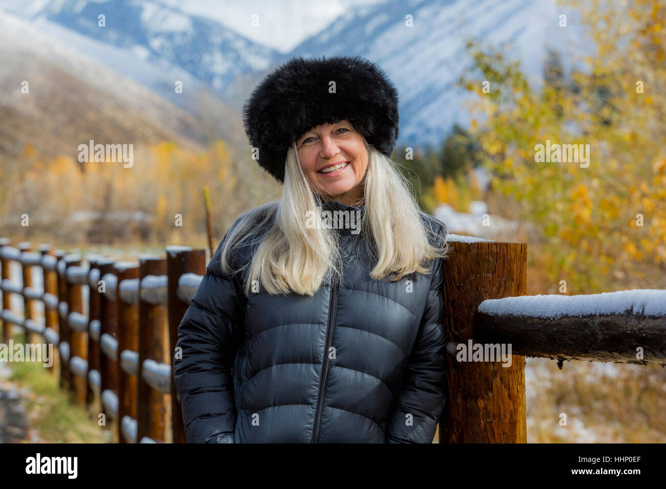 Caucasian woman wearing fur hat leaning on wooden fence in winter Stock Photo