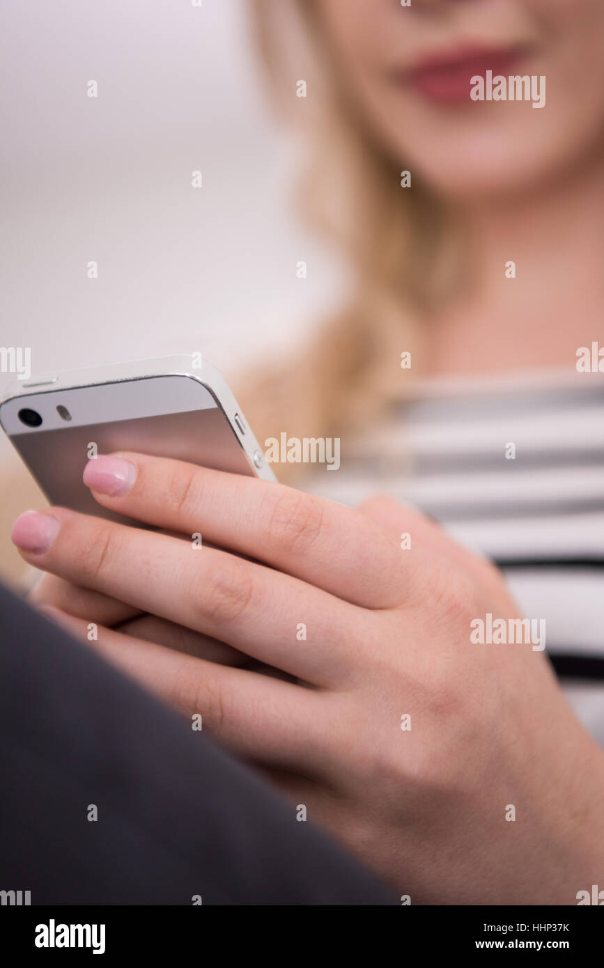 young happy woman sitting on sofa with mobile phone at luxury home ...