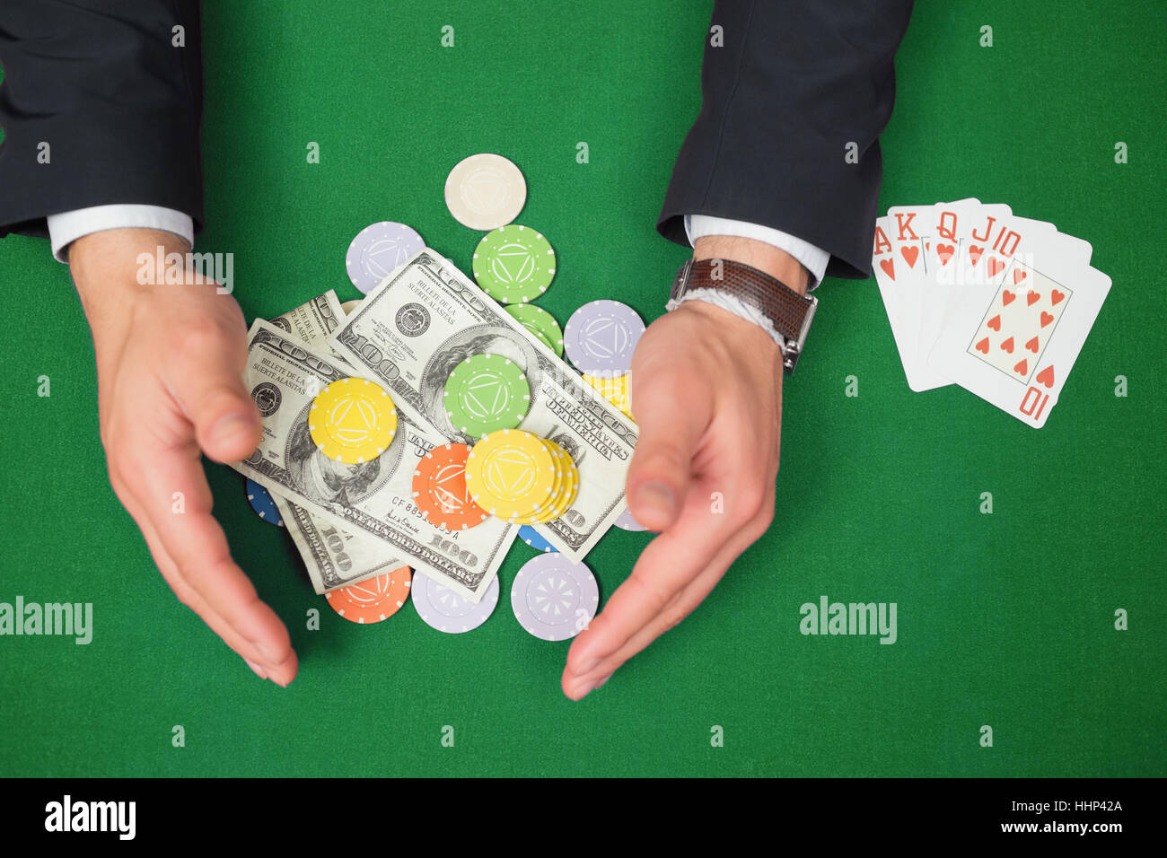 Hands grabbing dollars and chips from table beside royal flush in poker game Stock Photo