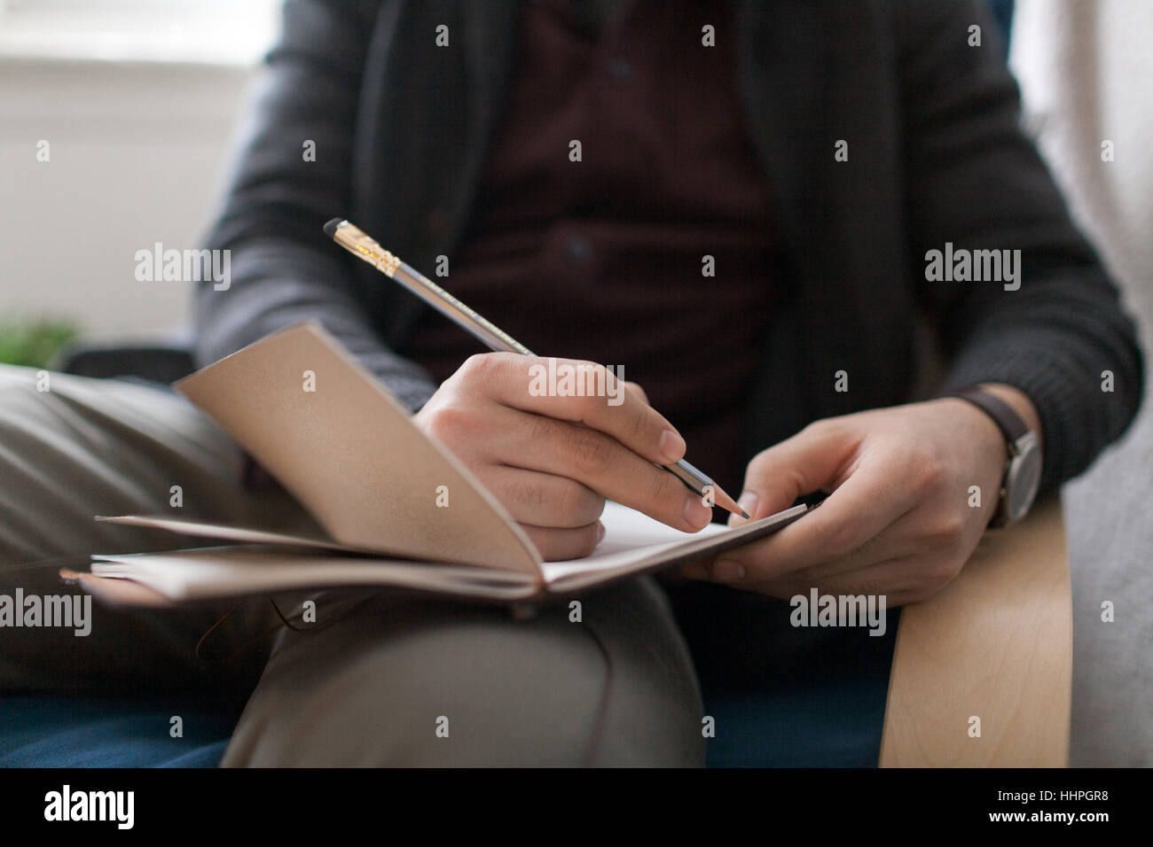 Young man sitting on a chair writing in his notebook with a pencil Stock Photo