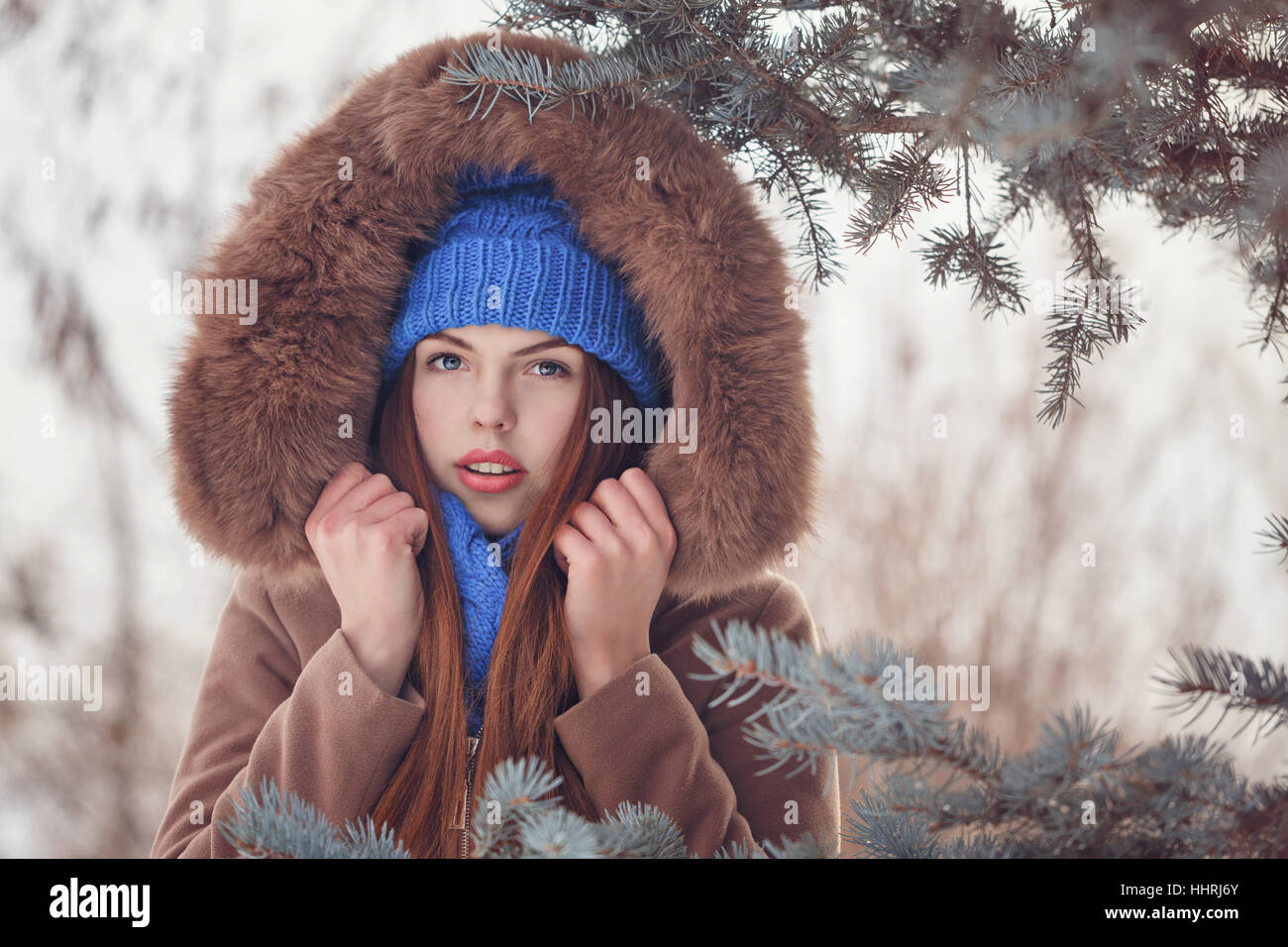 Cute teen girl in blue knitted hat and scarf walking in the park in winter. She wears a fur hood jackets. Outdoor Activities. Youth fashion. Close-up Stock Photo