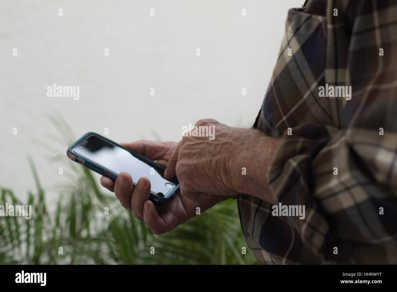 Man's hand holding cell phone in right hand standing outside over greens plants with negative space in upper left  background pointing to home button Stock Photo