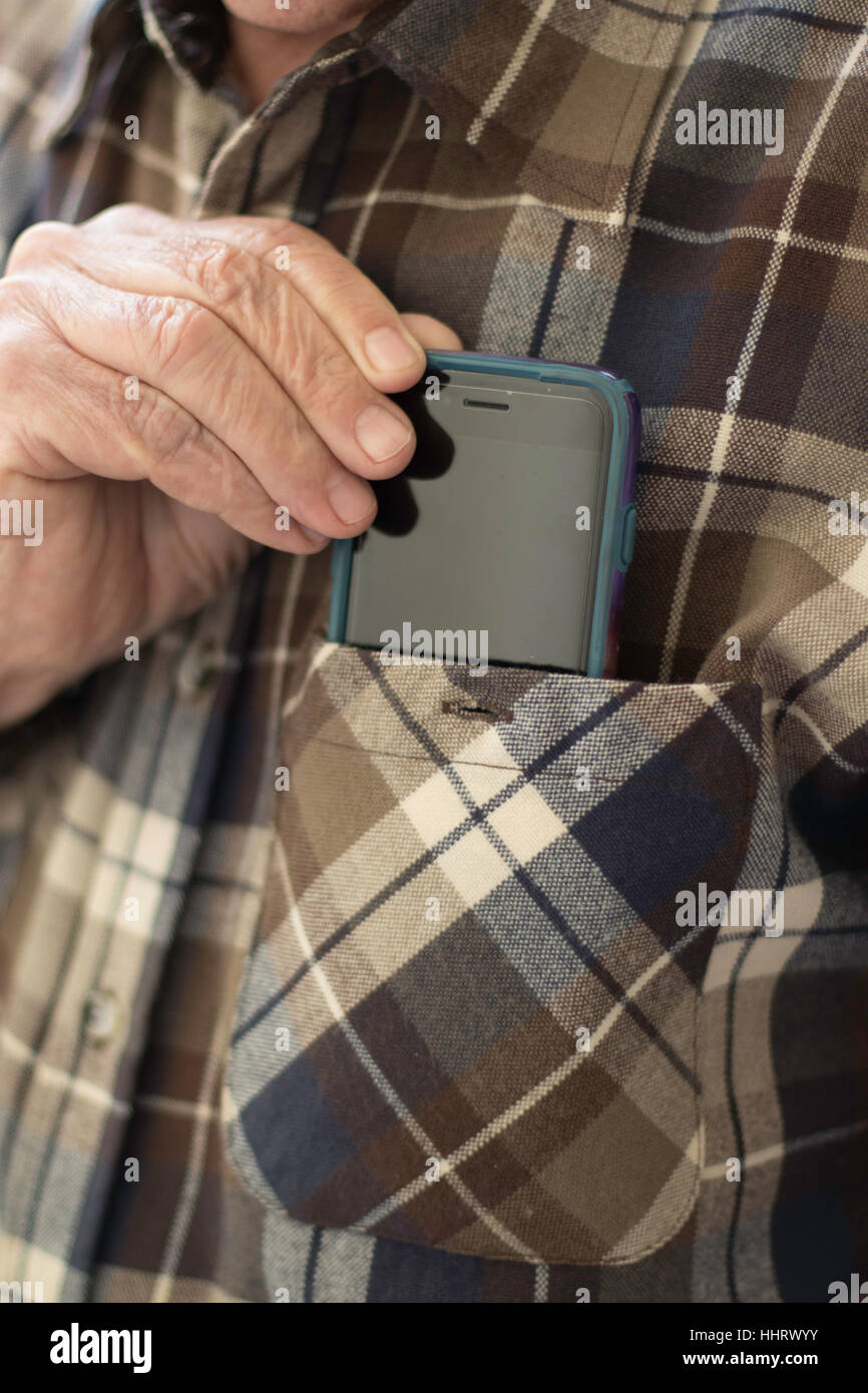 Man's hand with four fingers close together inserting mobile device into left front shirt pocket closeup in vertical format Stock Photo