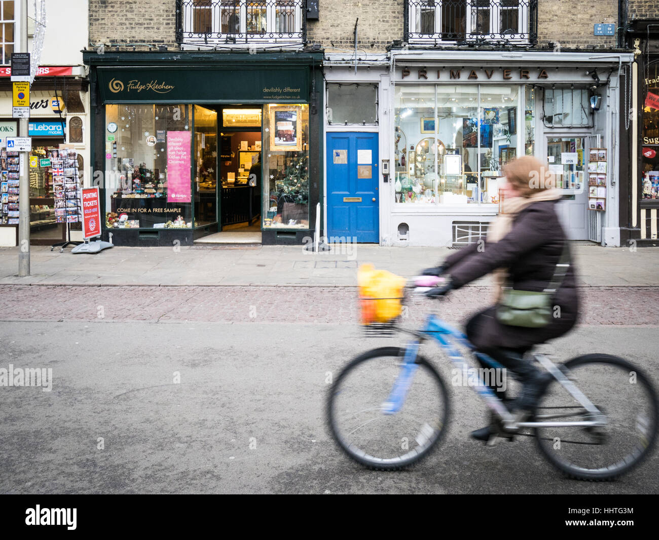 A woman cycles past independent shops in Cambridge UK Stock Photo