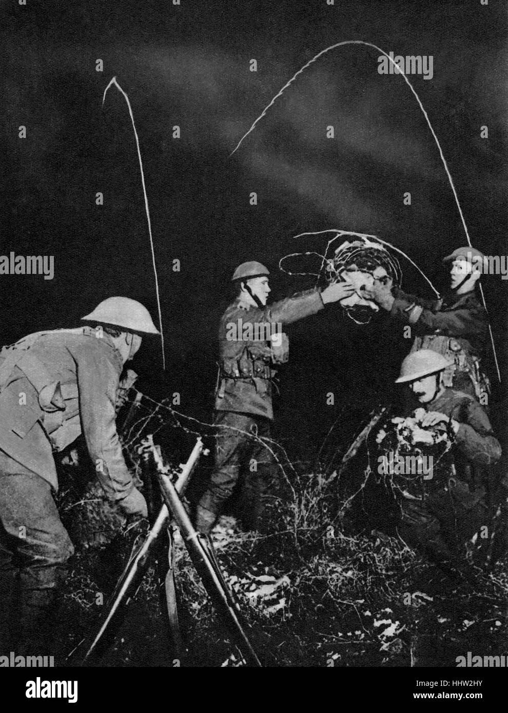 British soldiers erecting barbed wire entanglements in No Man's Land at night. Star shell flares seen behind. First World War, Stock Photo