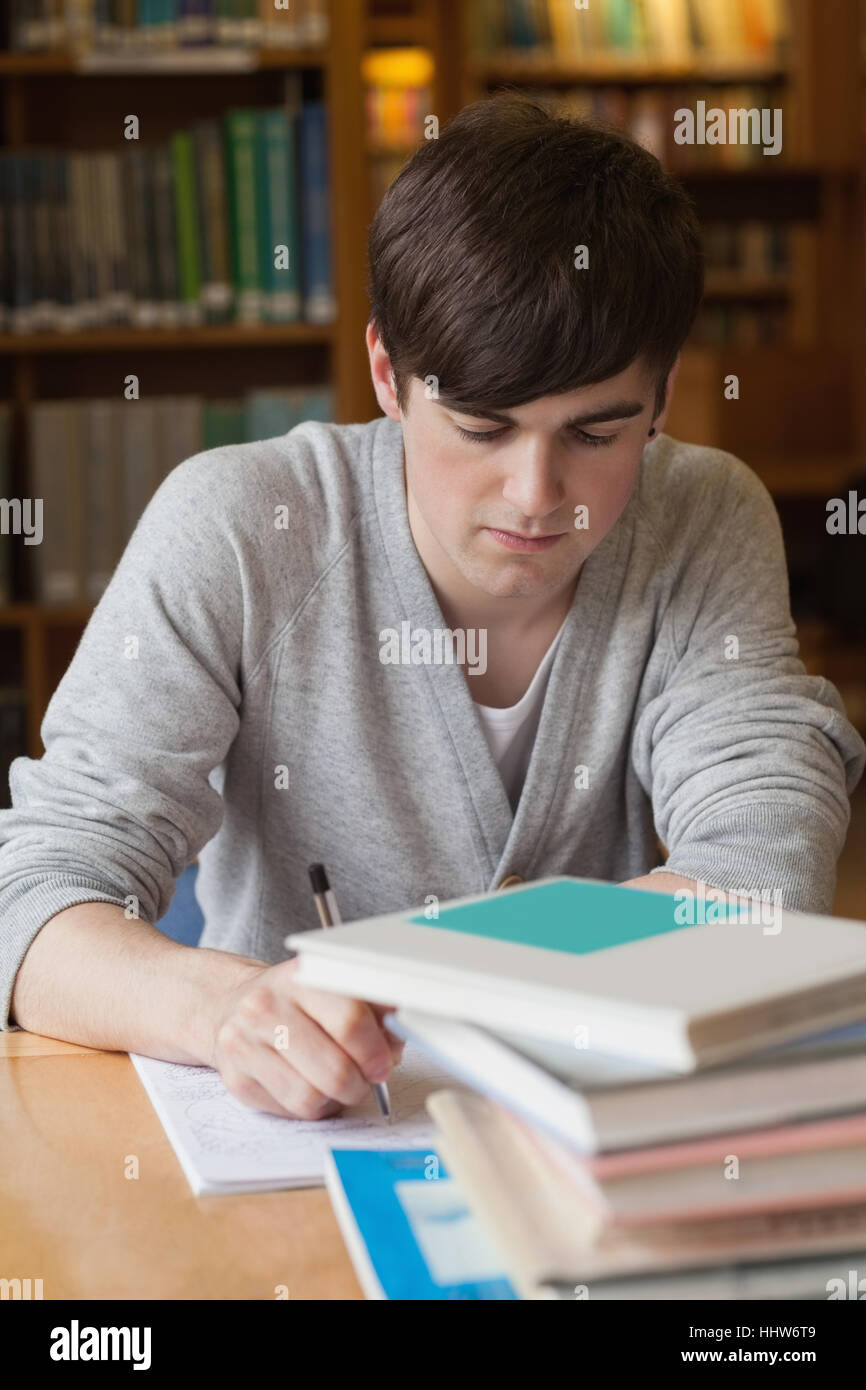 Man sitting at table at the library writing Stock Photo - Alamy