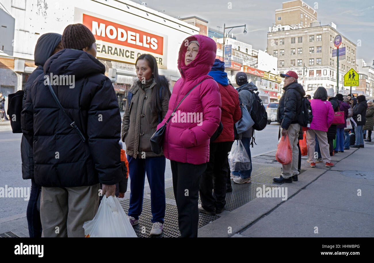 An Asian woman in a pink jacket in a crowd on a bus top on Roosevelt Ave, in Chinatown, downtown Flushing, Queens, New York Stock Photo