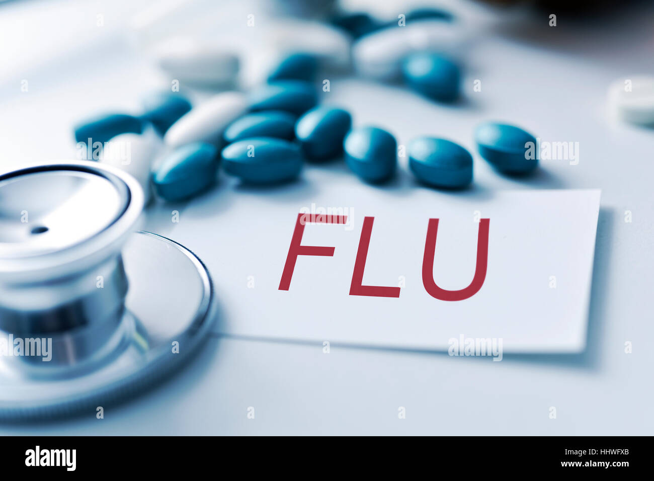 closeup of the desk of a doctors office with a stethoscope a bottle with pills and a piece of paper with the word flu Stock Photo