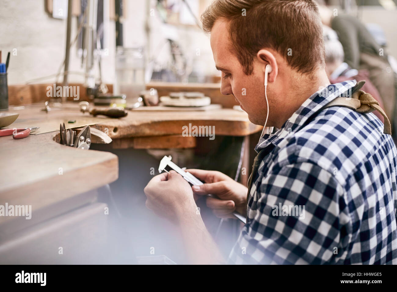 Male jeweler using calipers and listening to music with headphones in ...