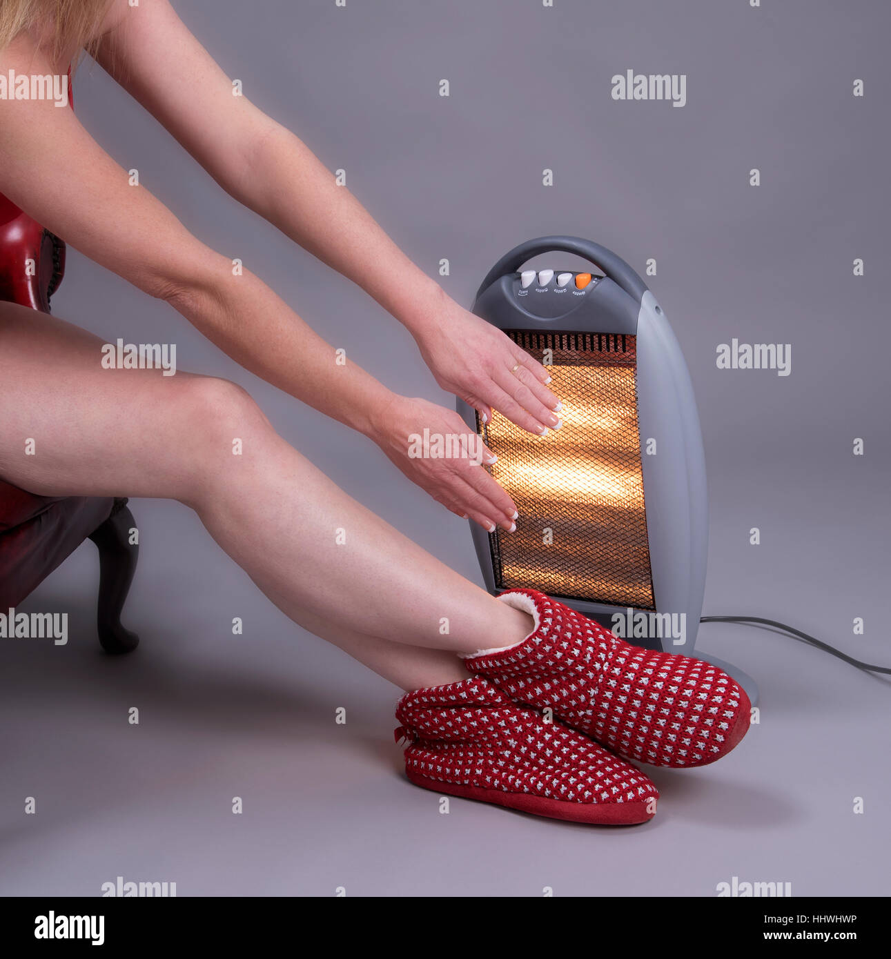 Woman with bare legs and arms warming her hands on an electric fire to