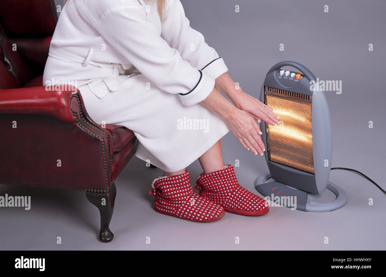 Woman in a dressing gown warming her hands in front of an electric fire