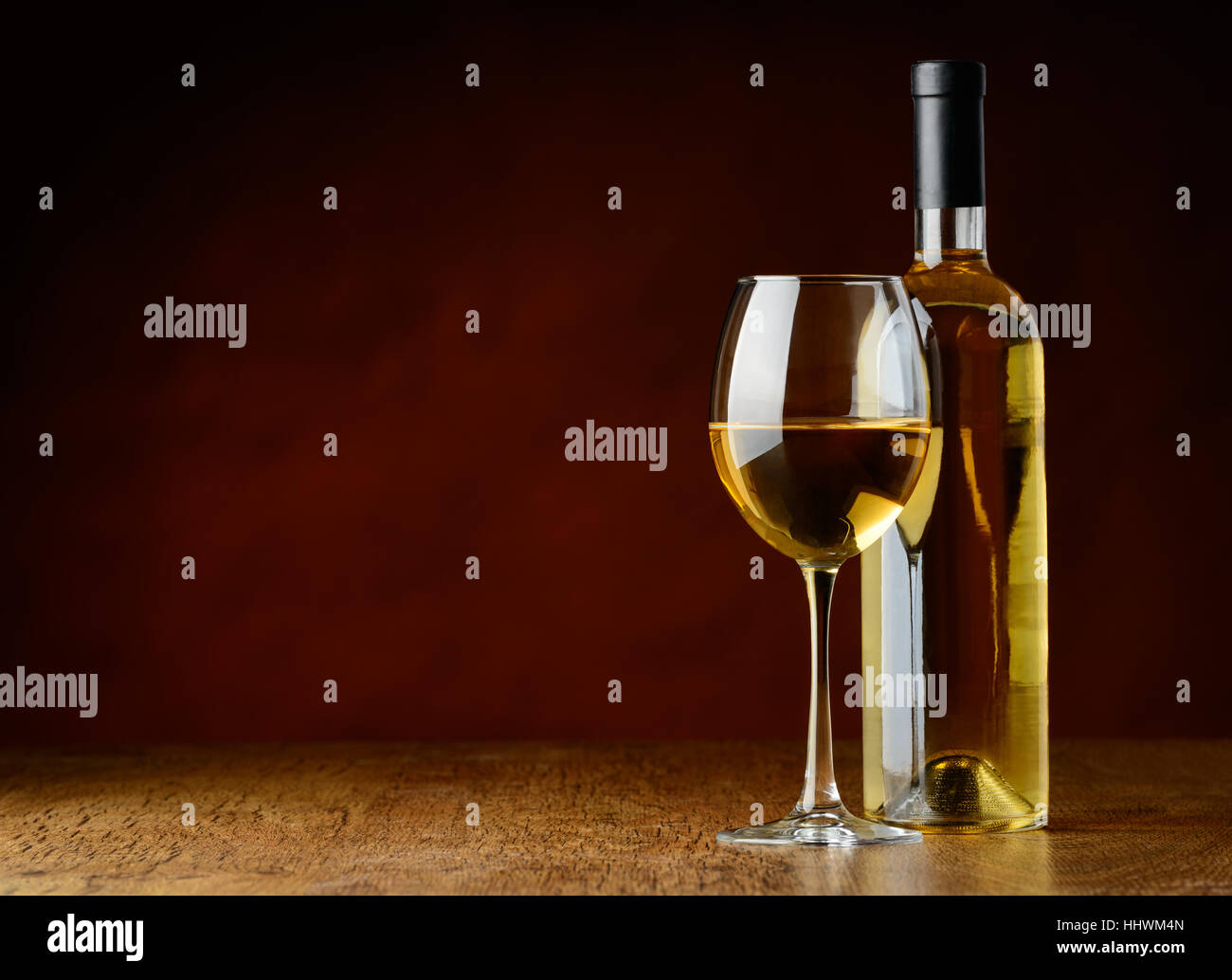 A glass of white wine and a bootle of white wine oni a wooden table in a a winecellar Stock Photo