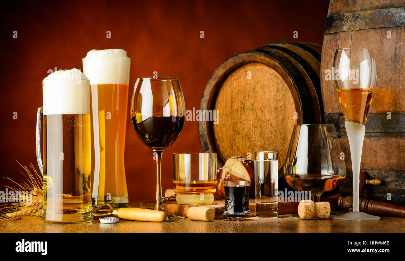 alcoholic drinks on wooden table in glasses, mugs and shots with barrel in background Stock Photo