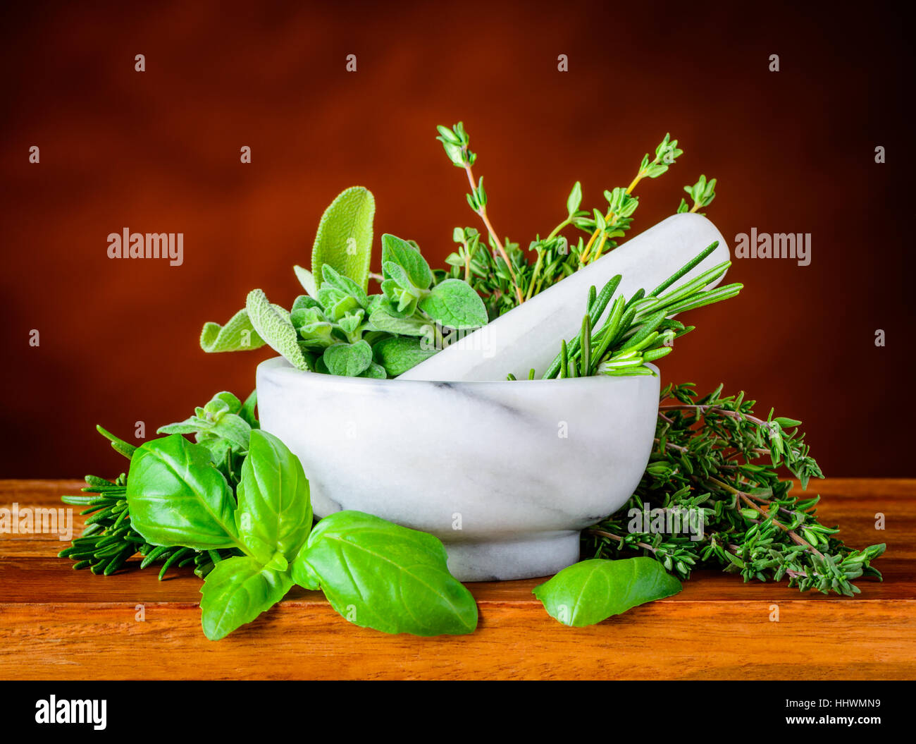 White pestle and mortar with different green herbs, basil, mint rosemary Stock Photo