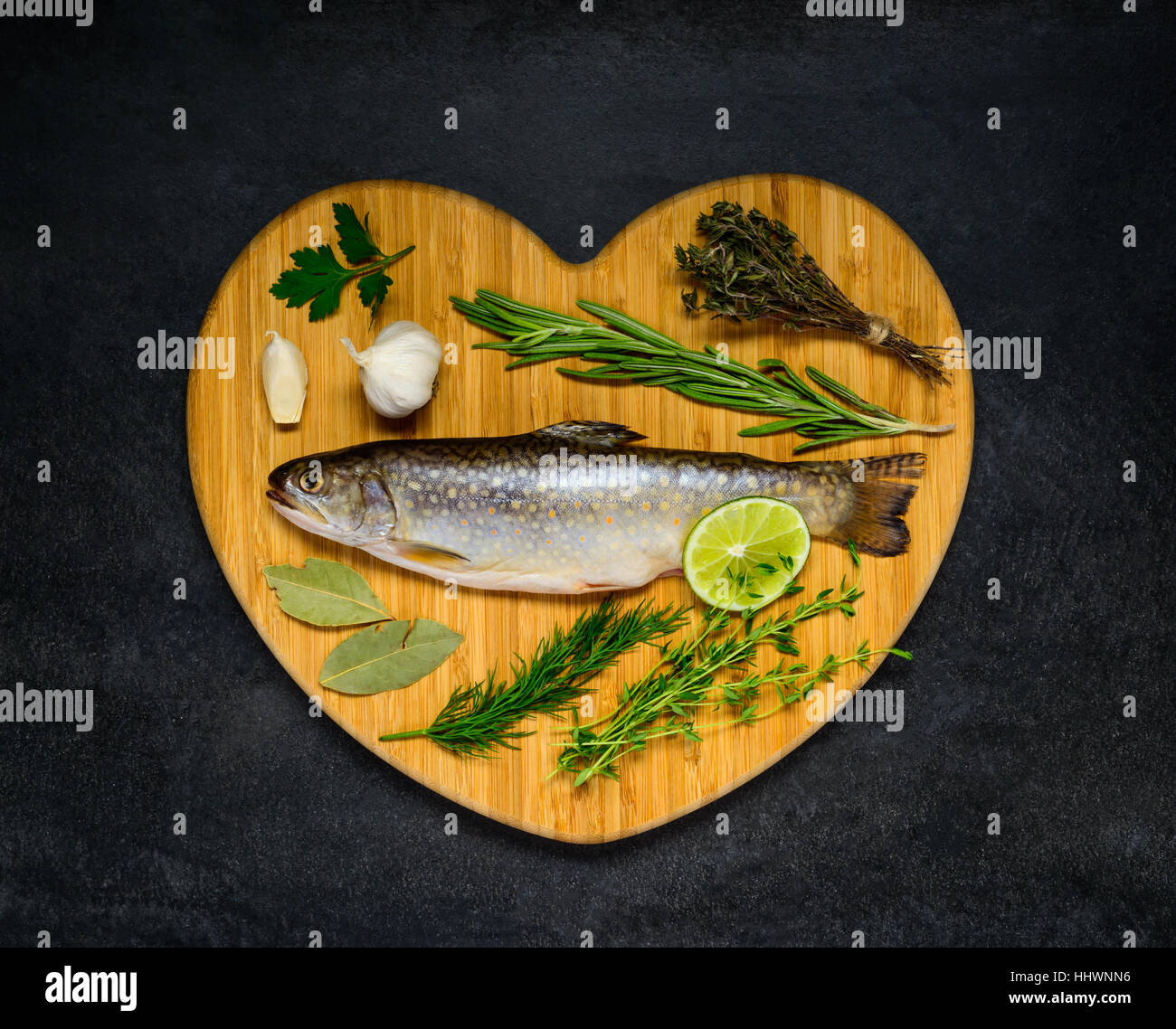 Raw Freshwater Rainbow Trout with cooking ingredients on heart shaped chopping board Stock Photo