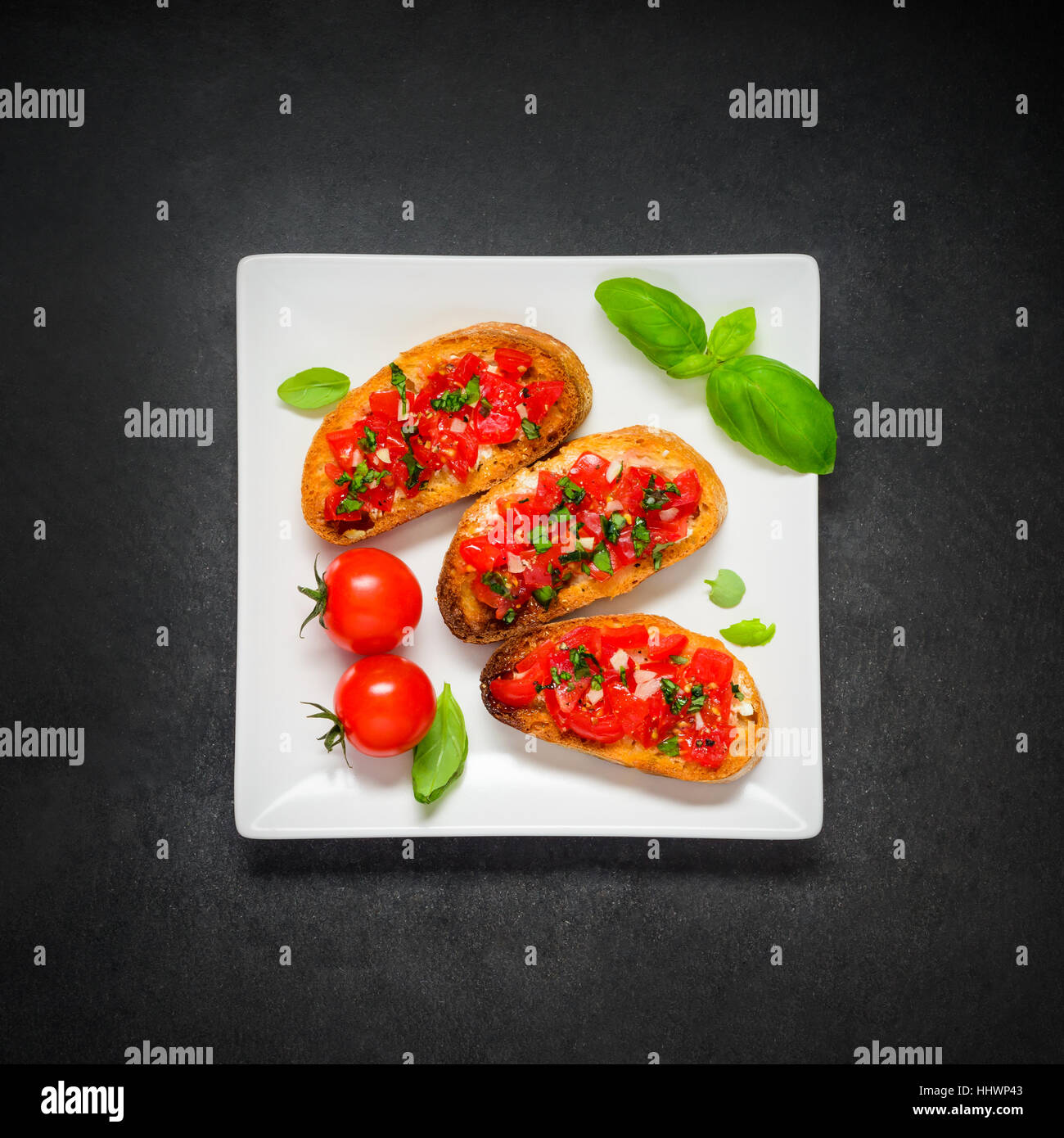Italian Cuisine Antipasto with Bruschetta, Tomatoes and Basil on White Plate Stock Photo