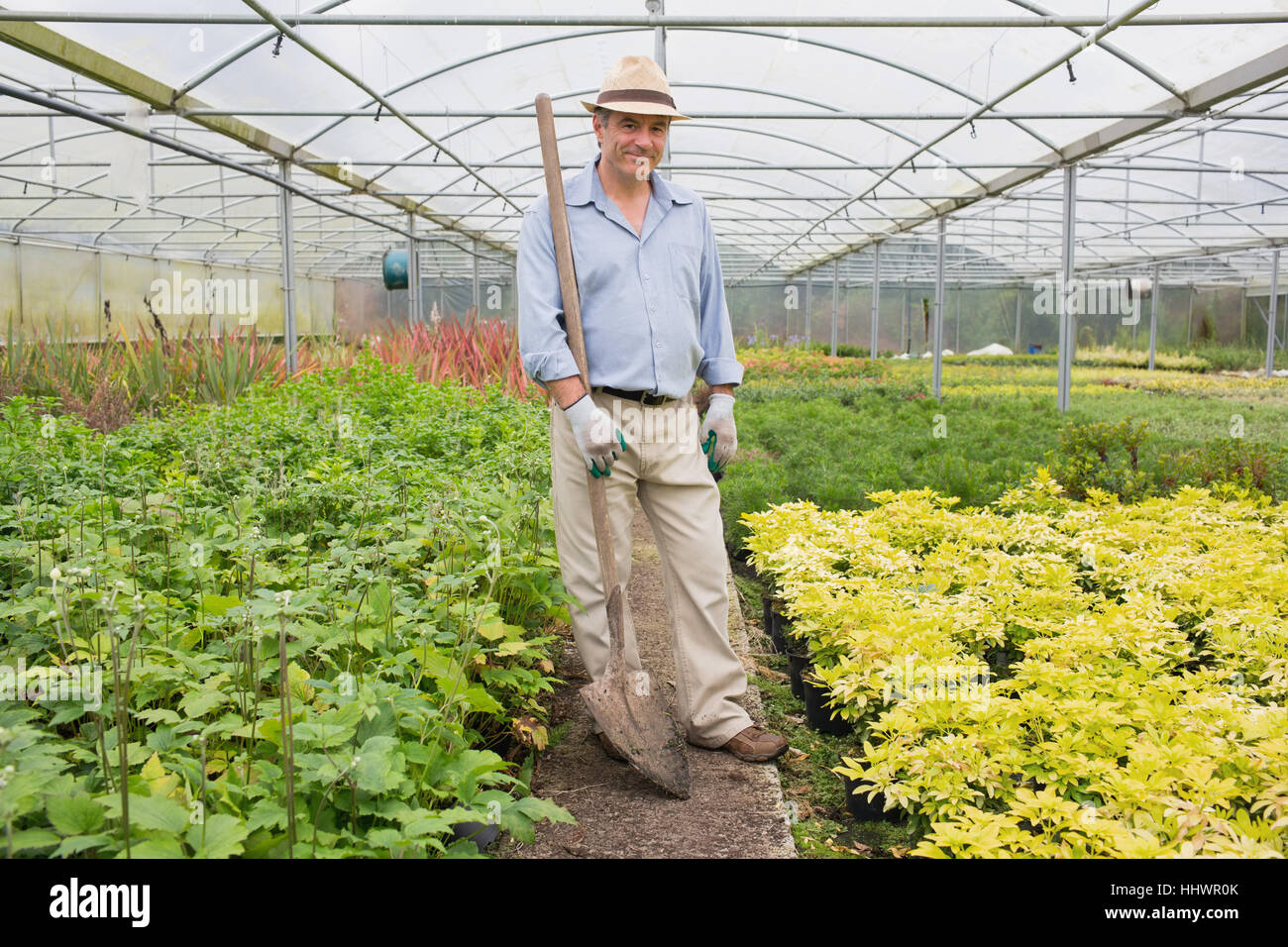 Man holding a spade while smiling and standing in the greenhouse Stock