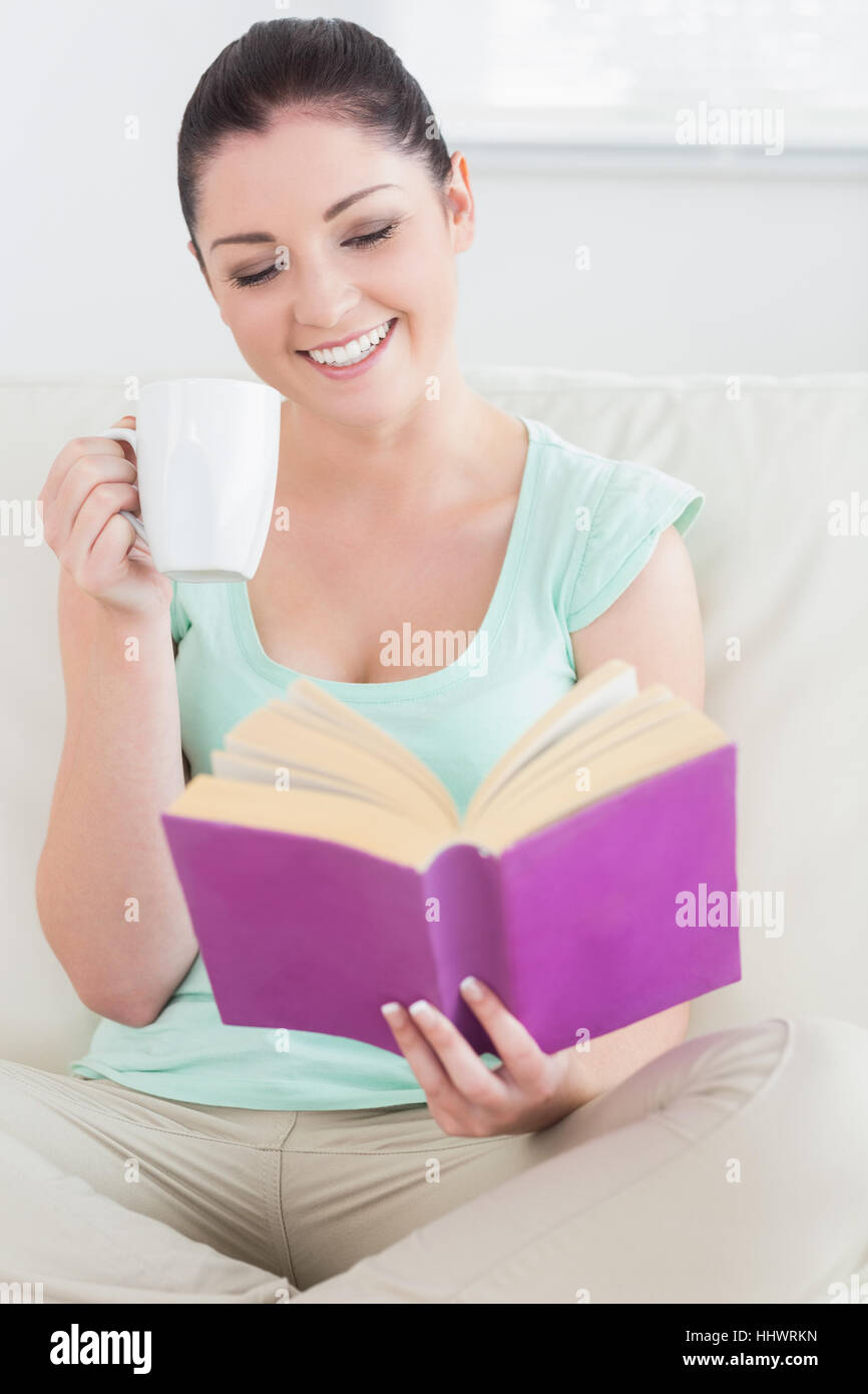 Woman sitting on the couch in a living room and drinking while reading