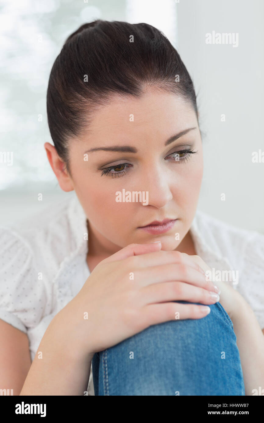 Thoughtful woman sitting on the couch in a living room and looking sad