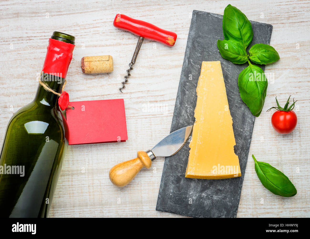 Yellow Parmigiano Reggiano Parmesan Hard cheese with basil and tomato. Bottle wine with corkscrew and cork. Italian cuisine Stock Photo