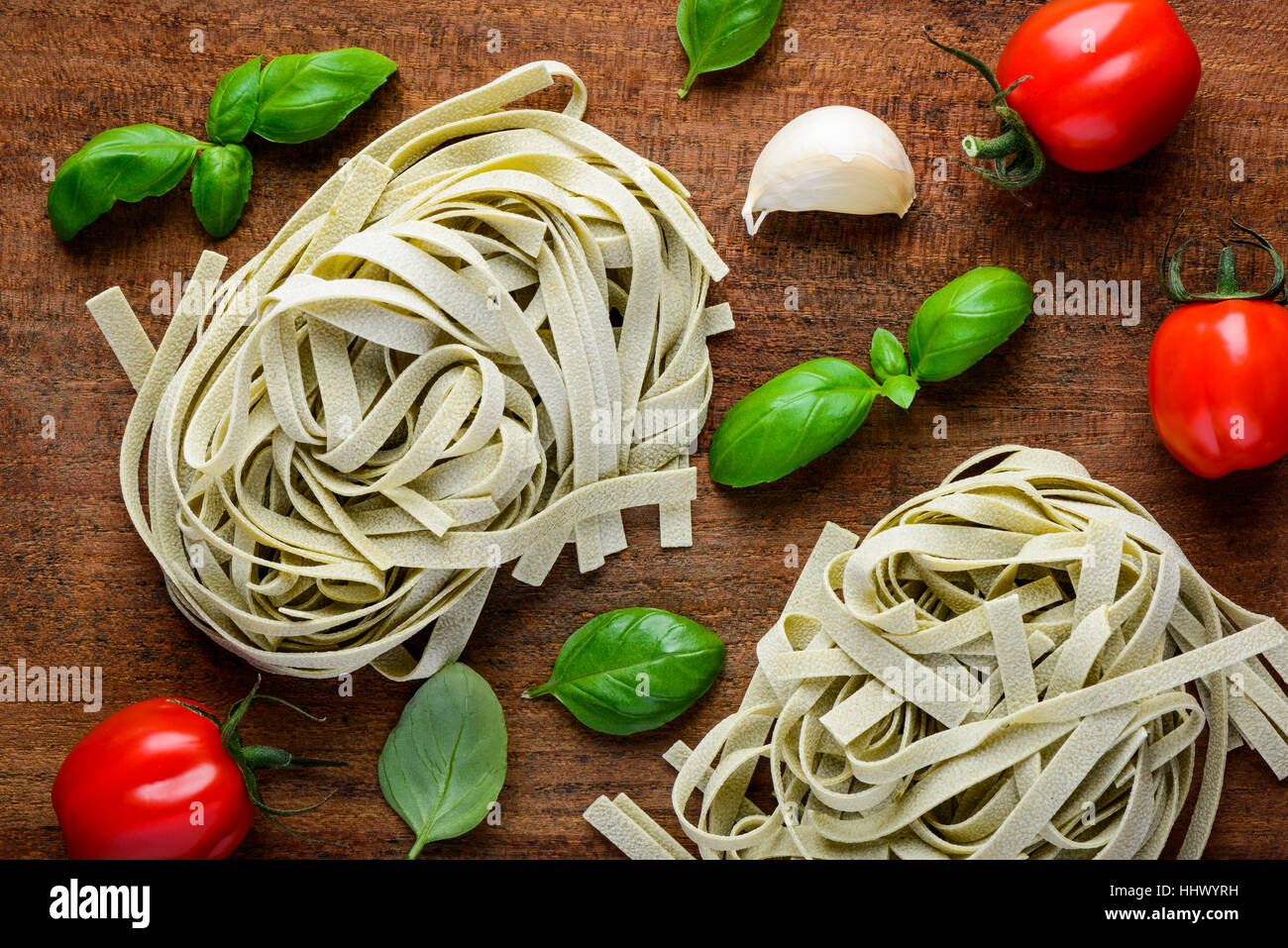 Green Tagliatelle tagliolini fettuccine with basil and tomato cooking ingredients. Stock Photo