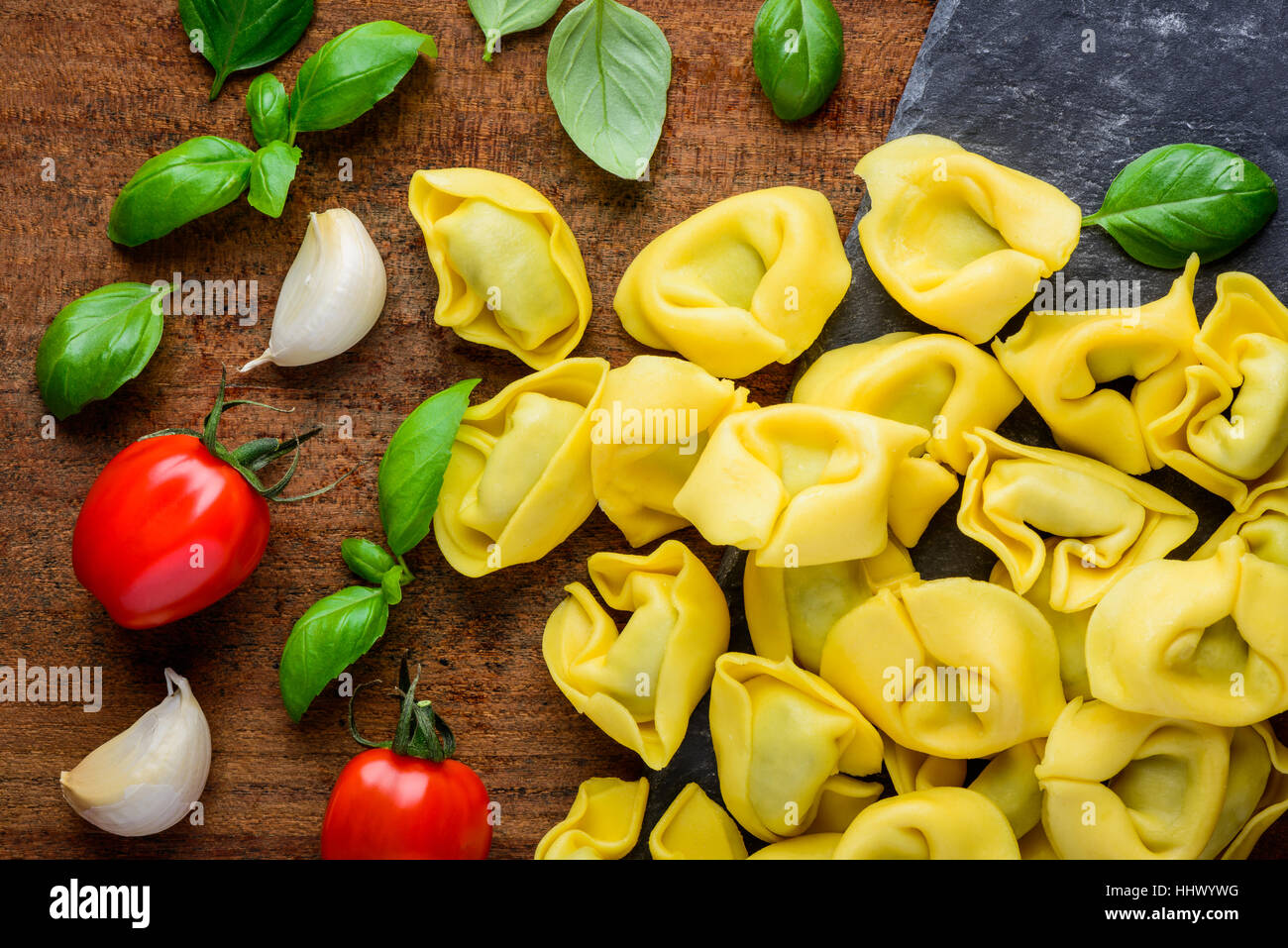 Yellow Tortellini Pasta with Green Basil Leaves, garlic cooking ingredients Stock Photo
