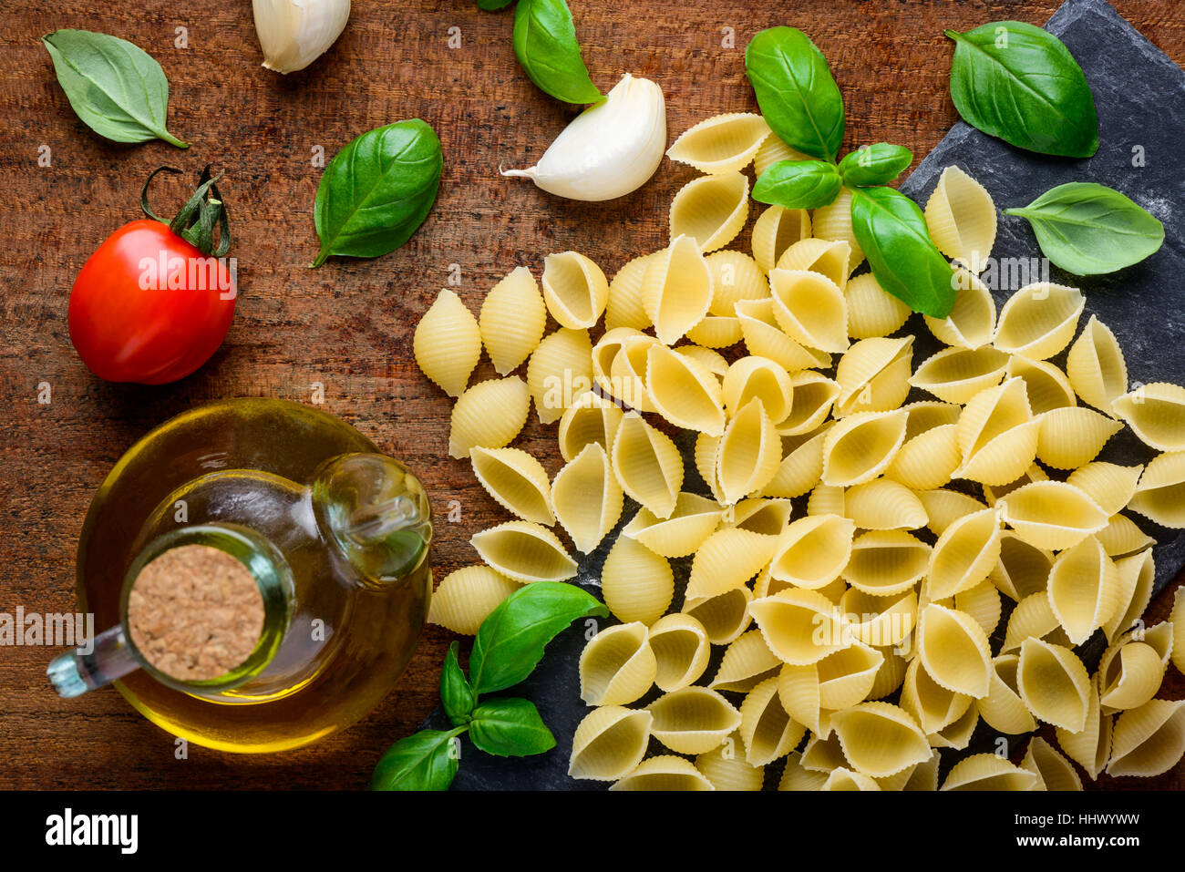 Yellow Conchiglie Rigate Pasta with cooking ingredients, basil, tomato and olive oil seasoning Stock Photo