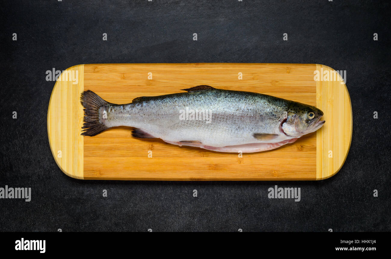 Raw Freshwater Trout Fish on Wooden Chopping board and on Dark Background Stock Photo