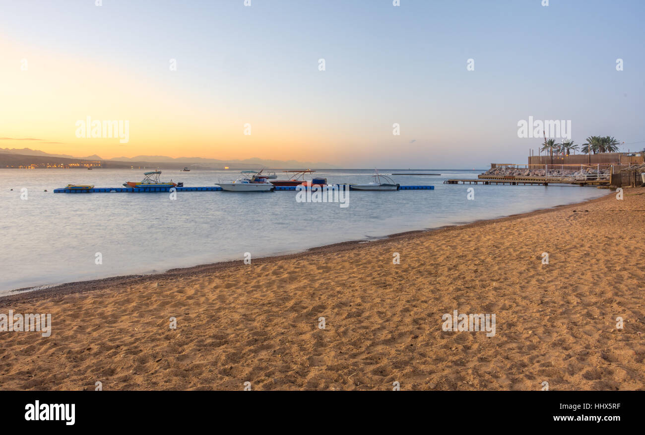 Boats at sunrise in the Gult of Aqaba with the mountains of Aqaba, Jordan in the back and the beach of Eilat, Israel in the front Stock Photo