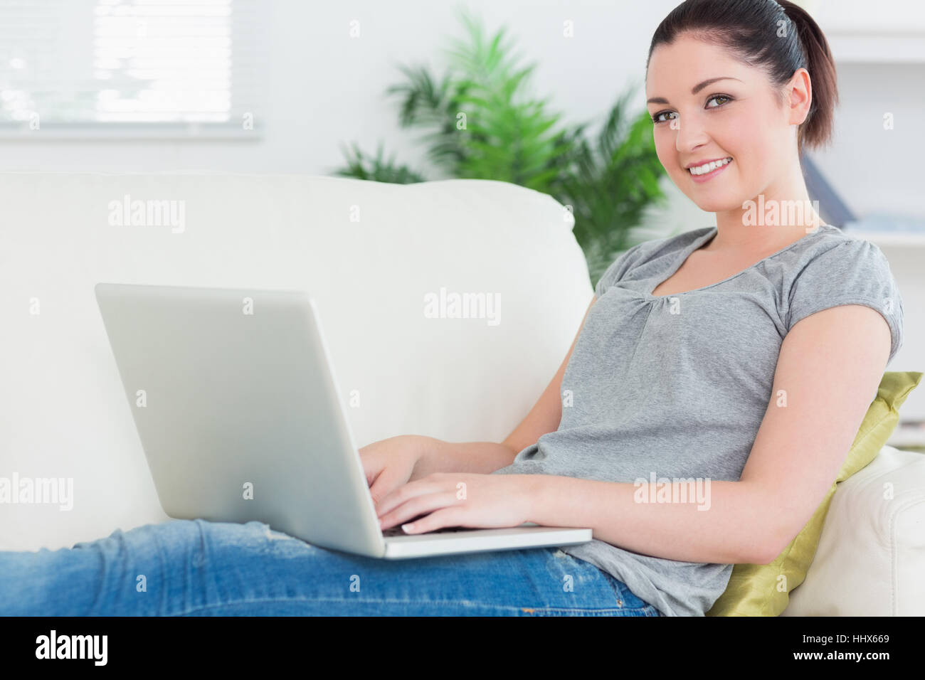Young woman sitting on the couch in a living room while using a laptop ...