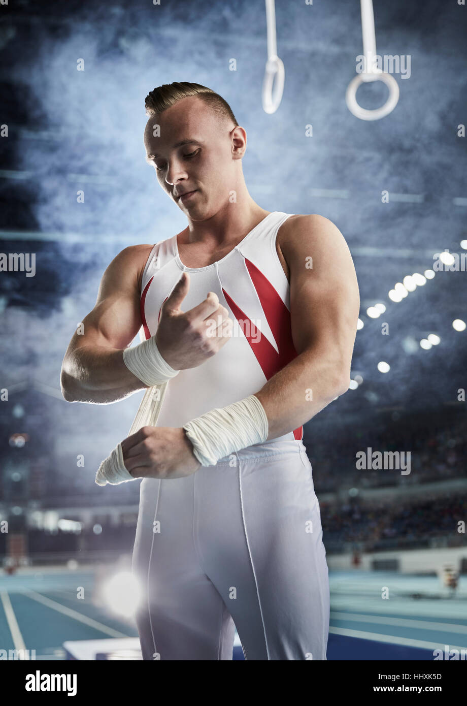 Male gymnast wrapping wrists below gymnastics rings in arena Stock
