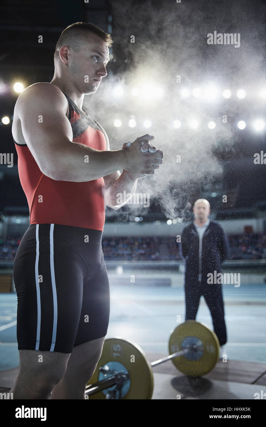 Coach watching male weightlifter applying chalk powder to hands at barbell Stock Photo