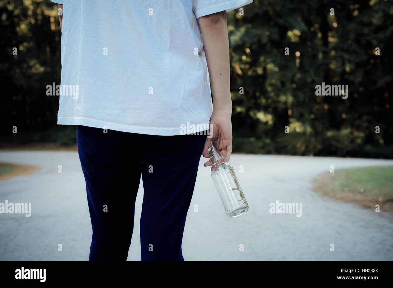 Teen girl standing at a fork in the road with a beer bottle Stock Photo